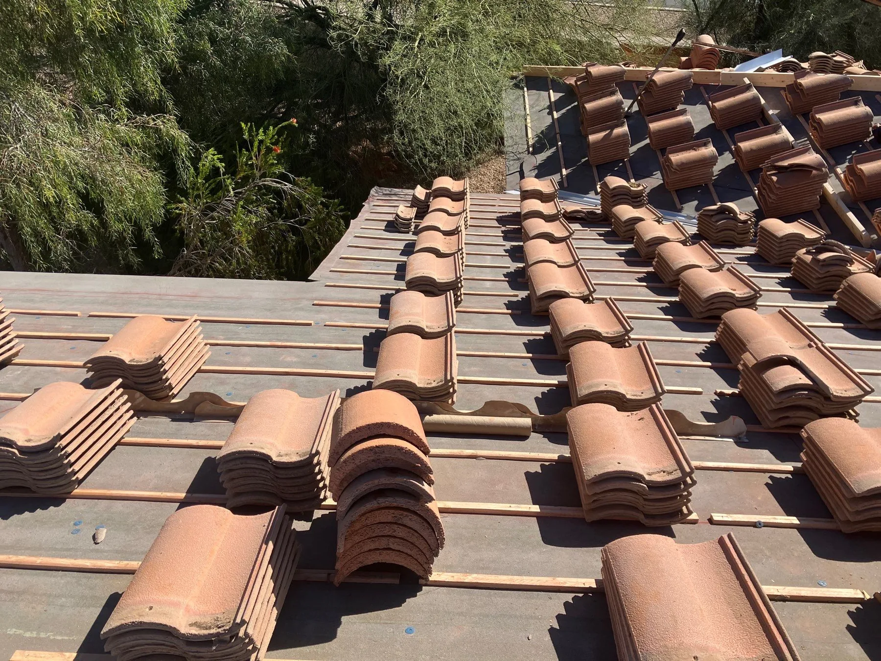 Close rooftop view of terracotta tile stacks over dark underlayment and battens near trees