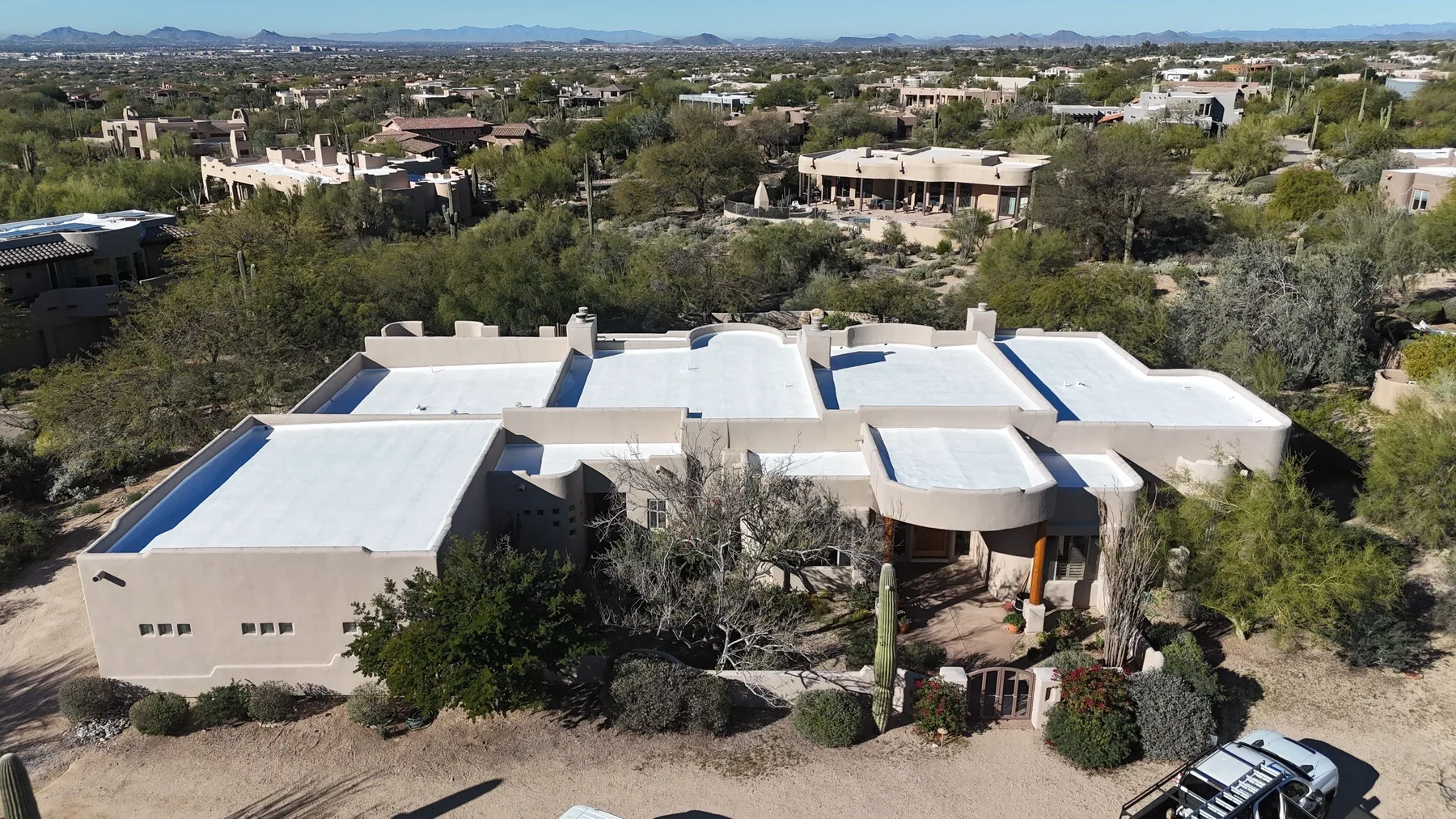 Wide aerial view of white flat and low-slope roofs amid dense desert landscaping