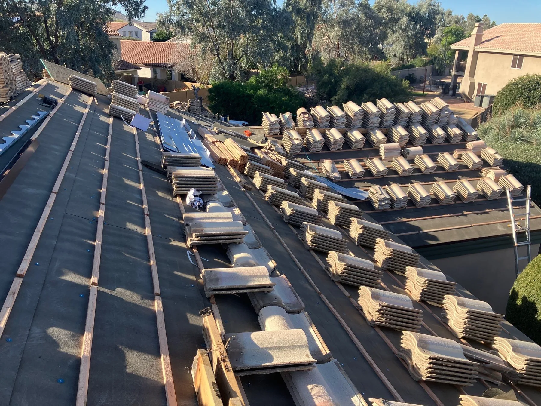 Steep rooftop view of tan tile bundles staged over black underlayment and battens