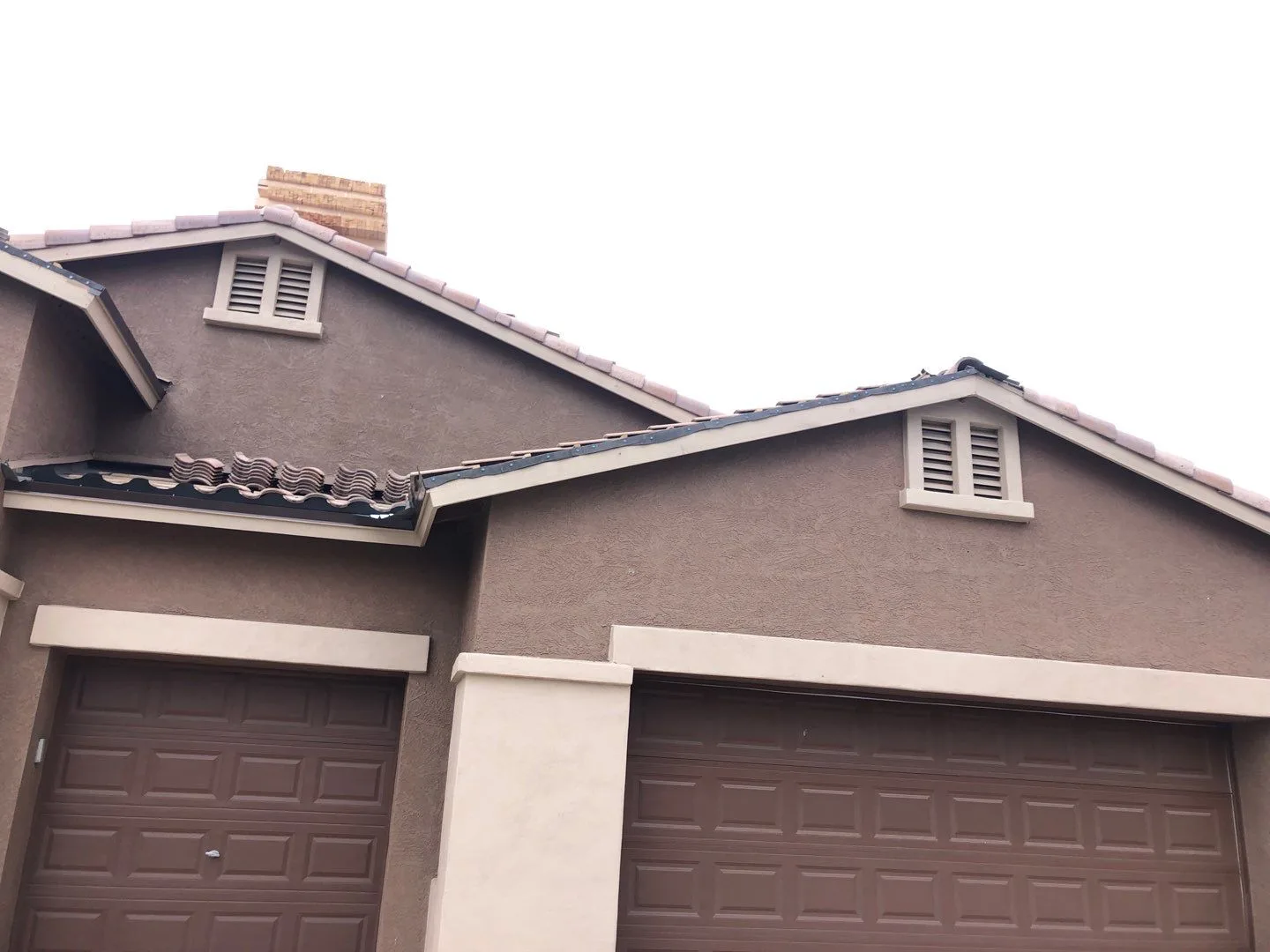 Street-level view of completed brown tile roofs above gray stucco garage gables