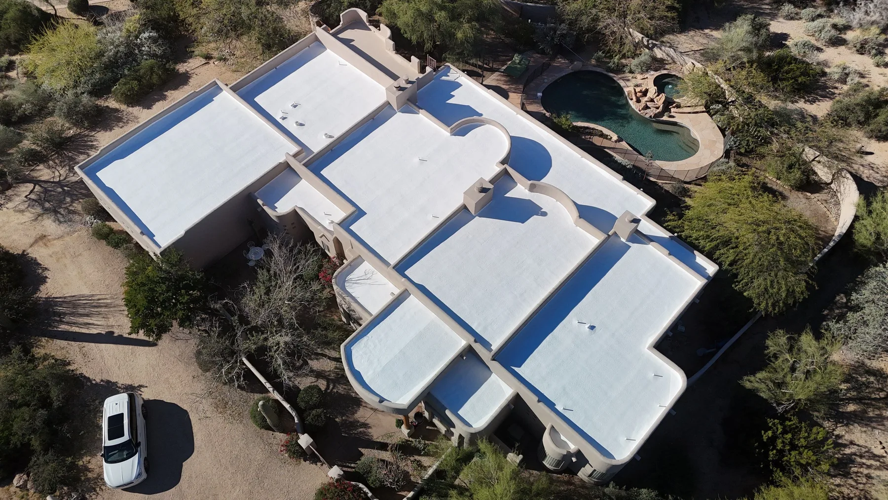 Top-down aerial view of white low-slope roofs with curved sections beside a swimming pool