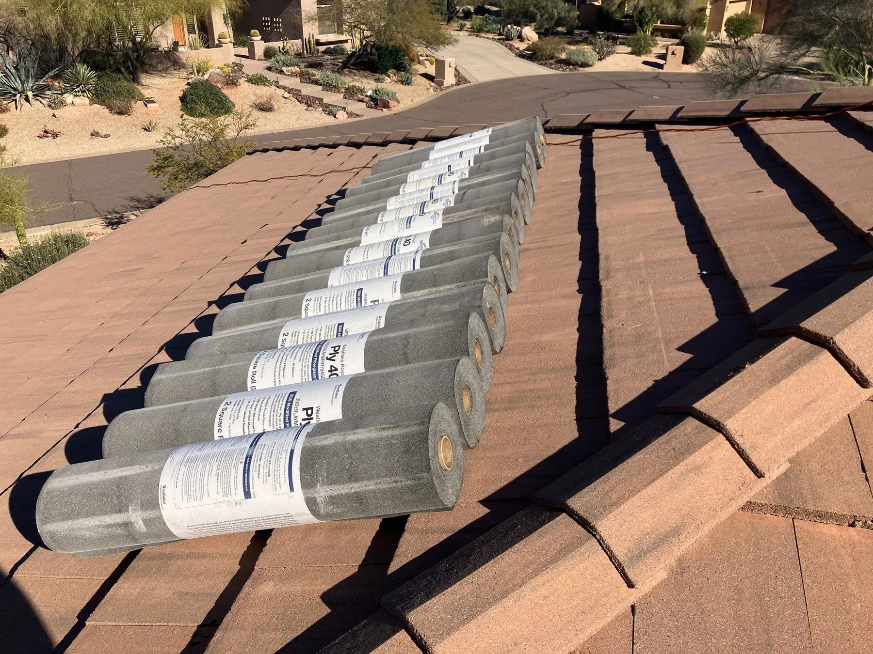 Rooftop view of gray wrapped rolls staged along a reddish-brown tiled slope