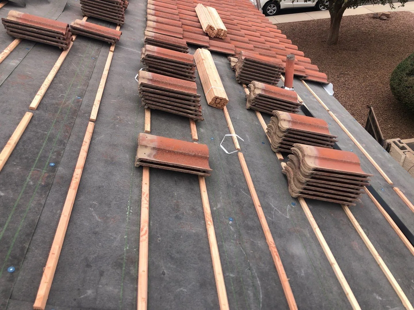 Angled overhead view of black roof underlayment, wood battens, and stacked red tiles