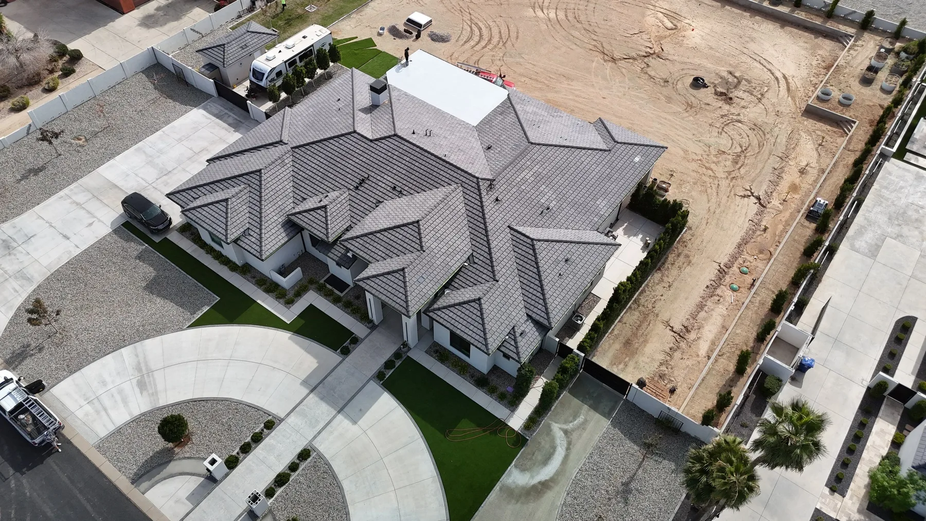 High aerial view of completed gray tiled hip roof with white flat sections and driveway