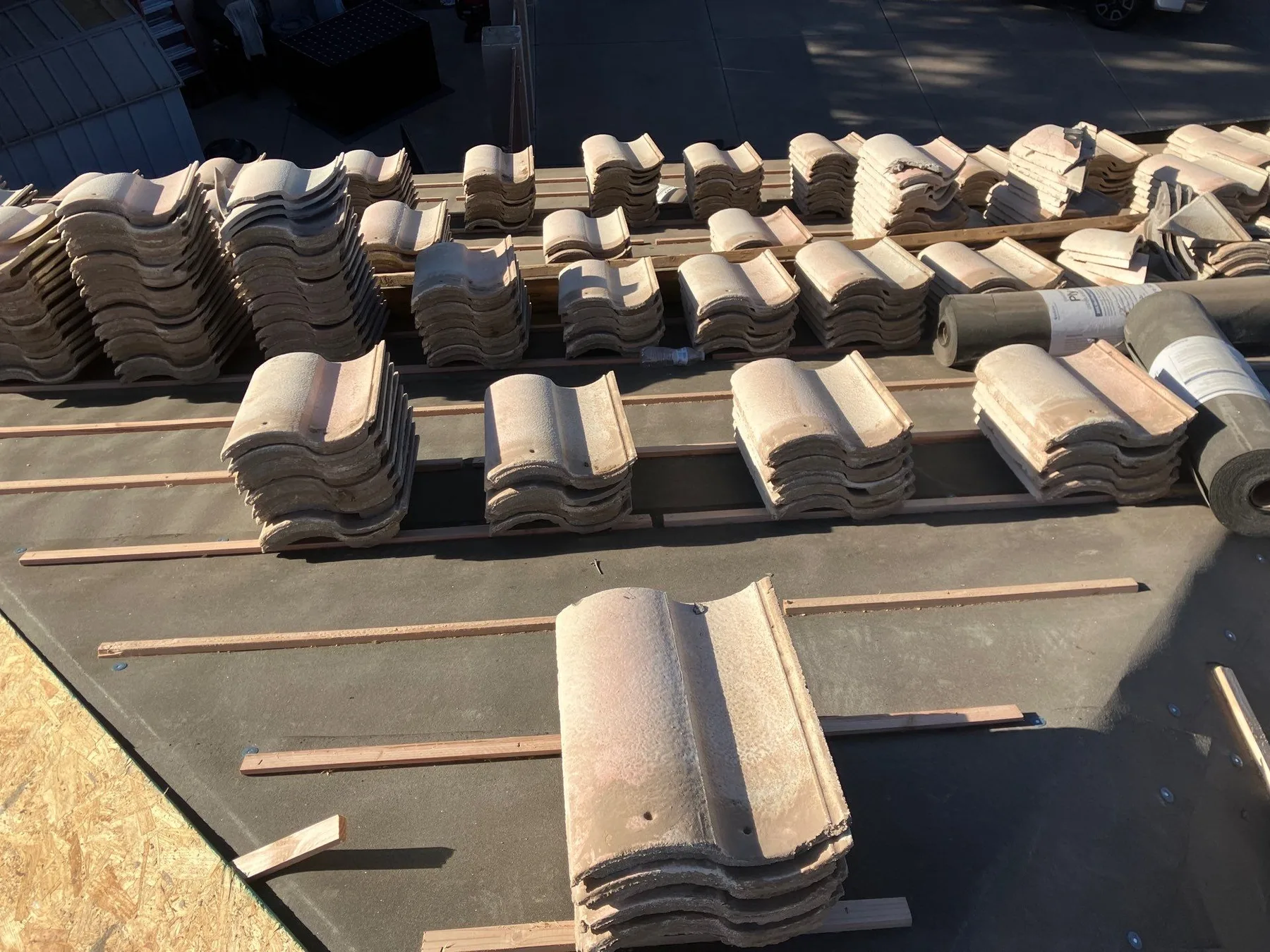 Close overhead view of stacked beige curved tiles across dark underlayment and wood battens