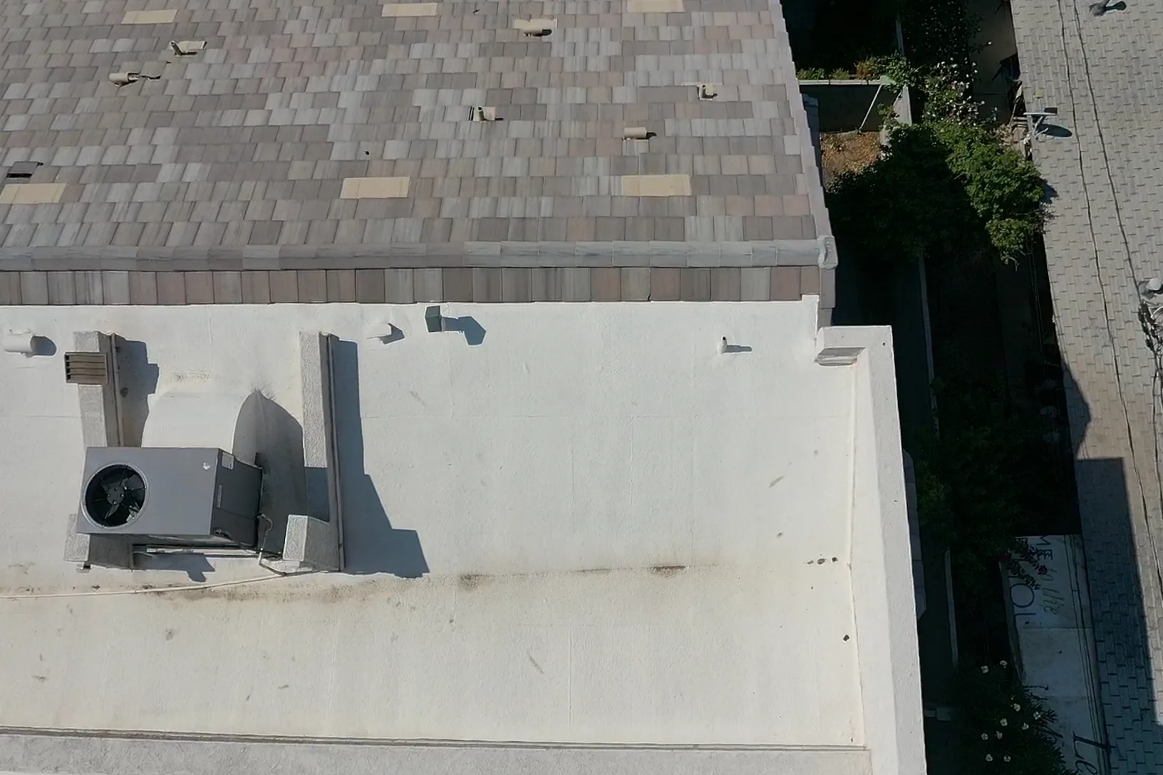 Top-down view of white flat roofing meeting brown shingles with a large rooftop unit