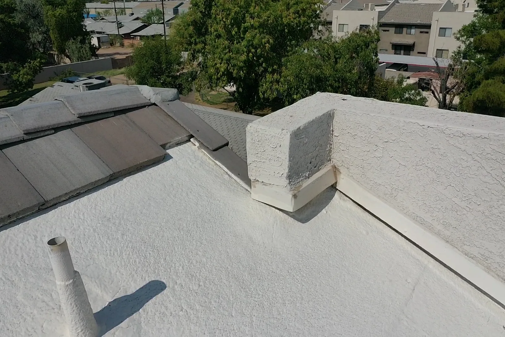 Oblique close view of white coated flat roofing with parapet curb, pipe, and dark transition