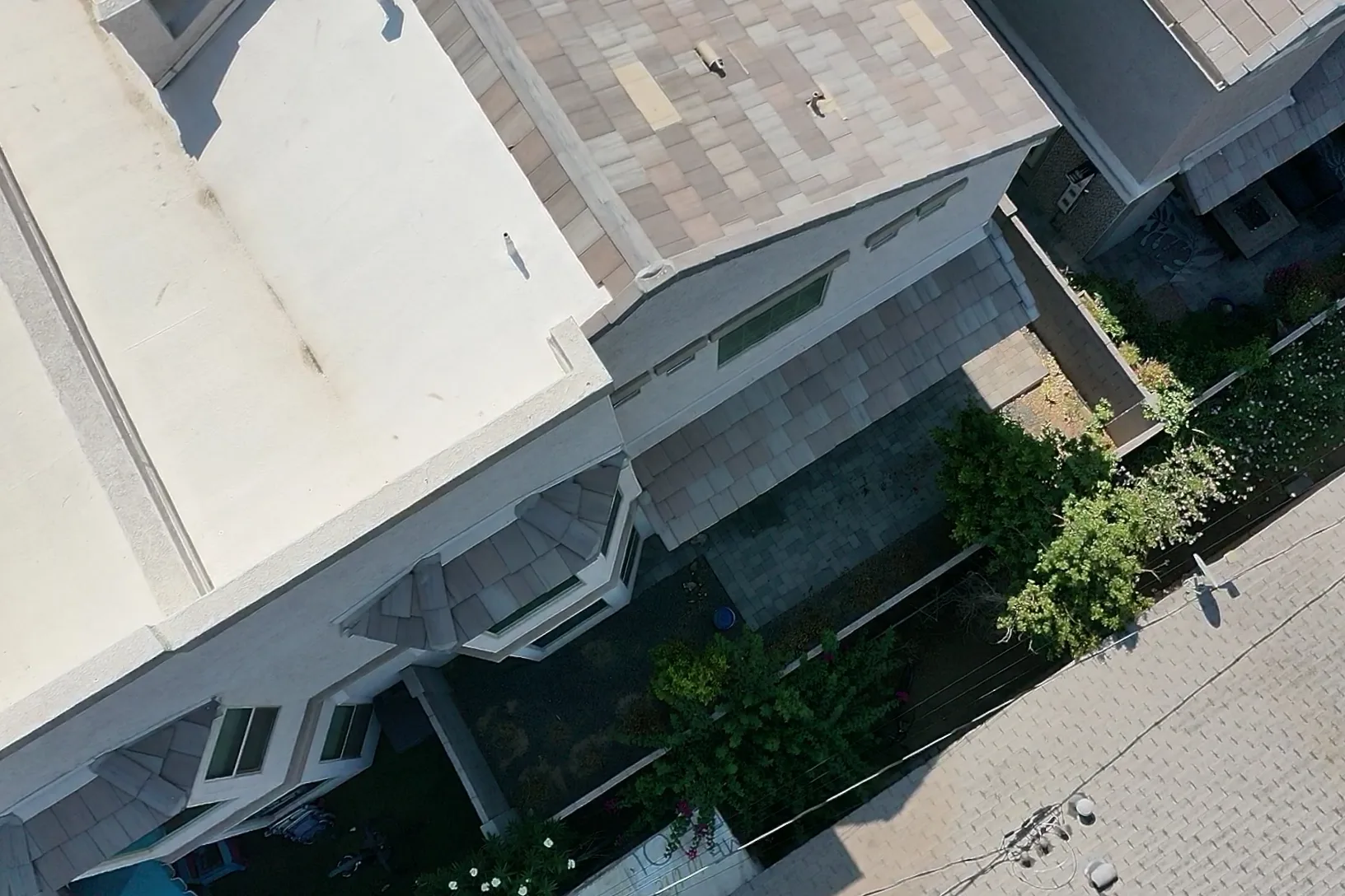 Steep aerial view of white flat roofing transitioning to pale variegated shingles above balconies