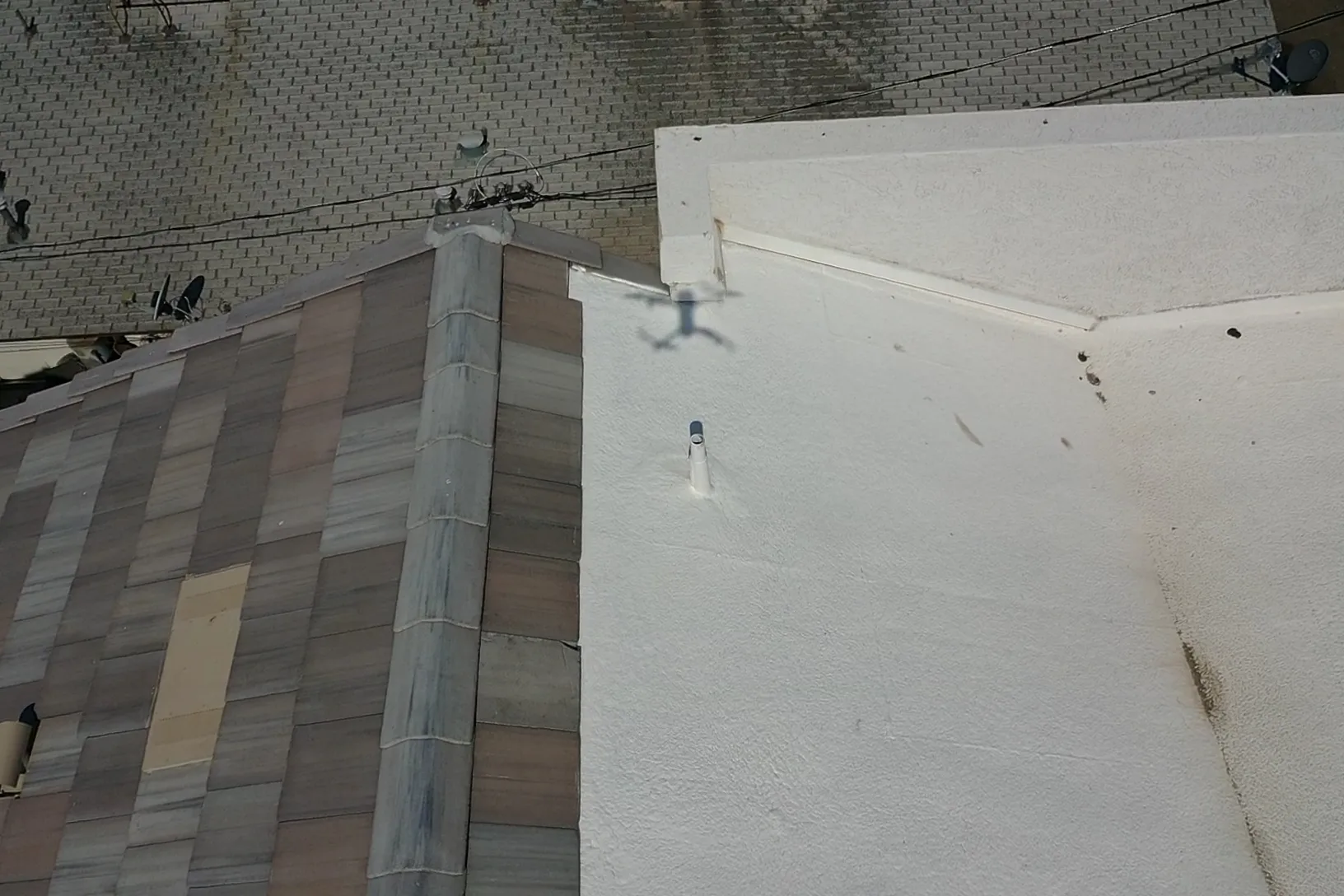 Overhead view of white coated low-slope roofing beside multicolored shingles and raised parapet