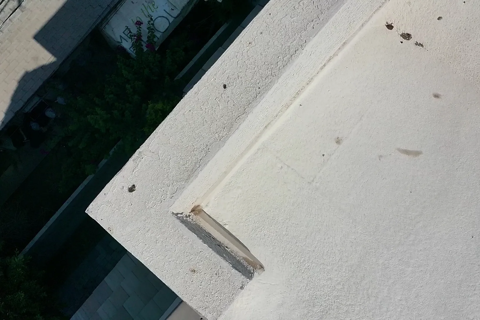 Steep overhead close-up of white coated roof edge with raised seam and scattered debris