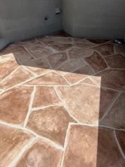 Downward view of finished reddish stone-pattern walk deck enclosed by gray walls and sunlight