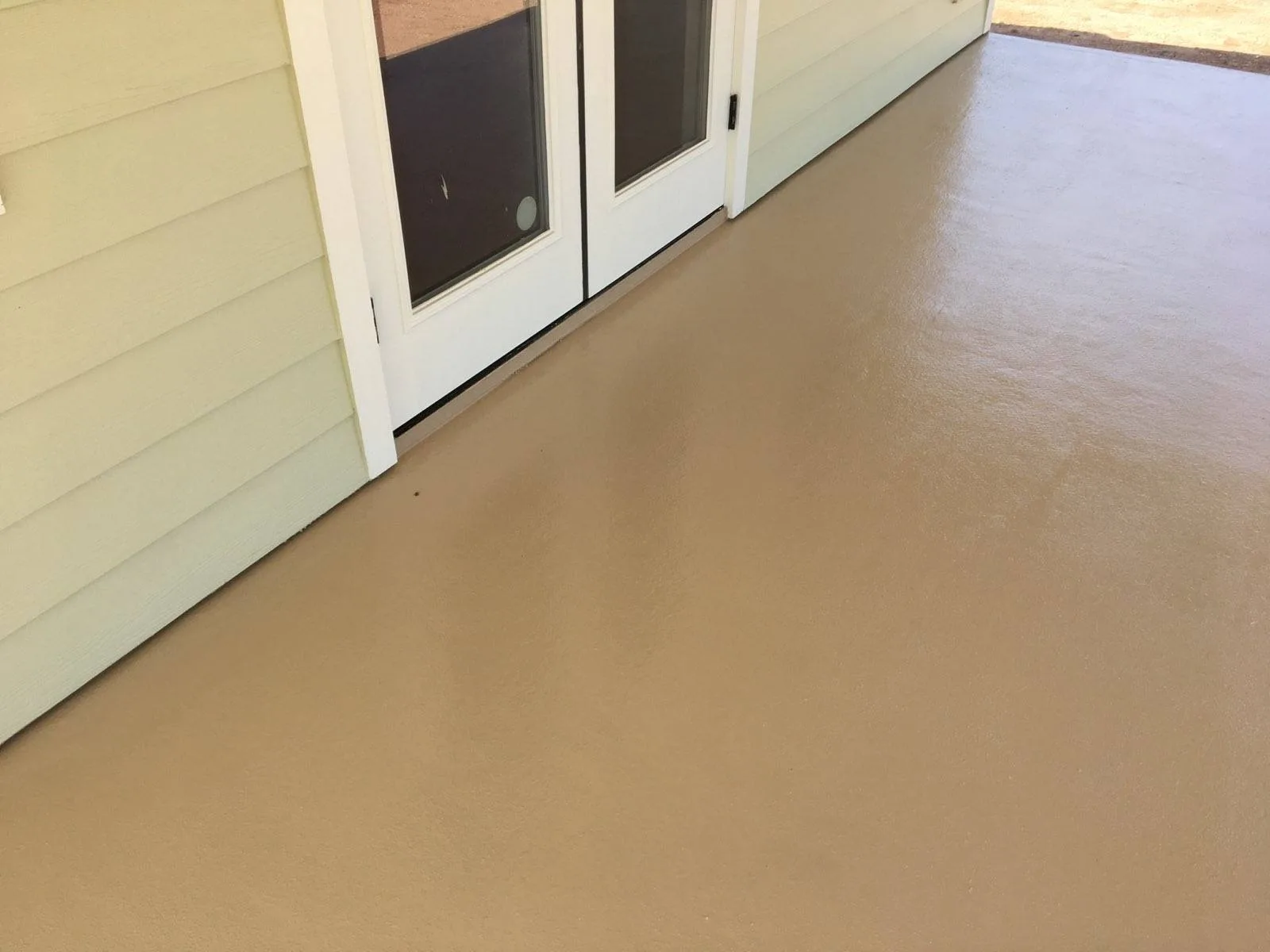 Oblique view of tan coated porch outside white doors and pale yellow siding