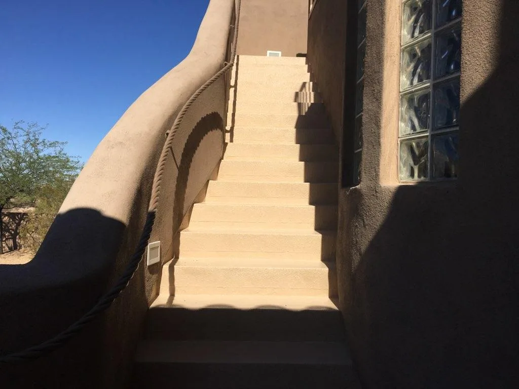 Upward view of beige coated exterior stairs with curved stucco railing