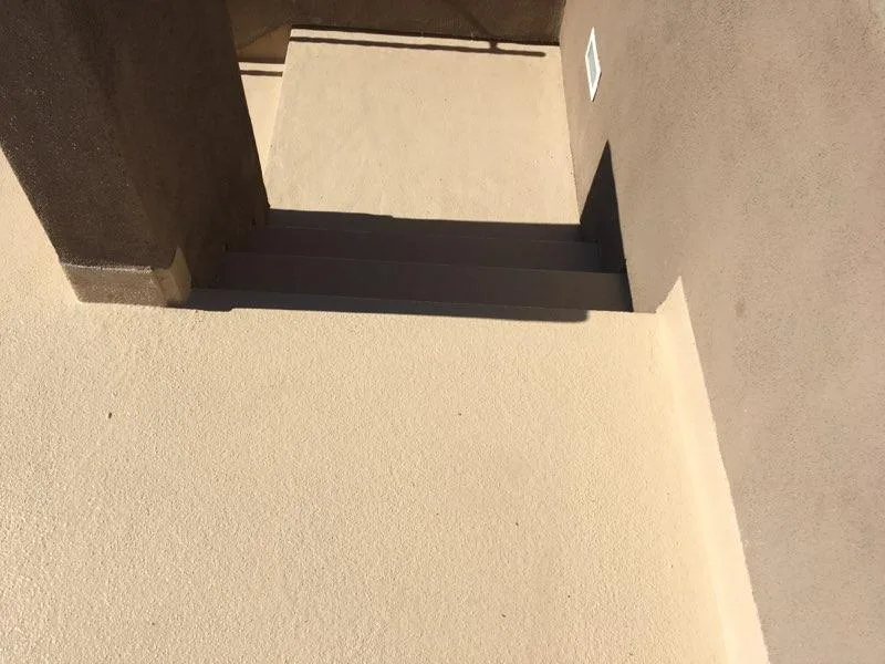 Downward view of beige textured landing and dark steps enclosed by brown stucco walls