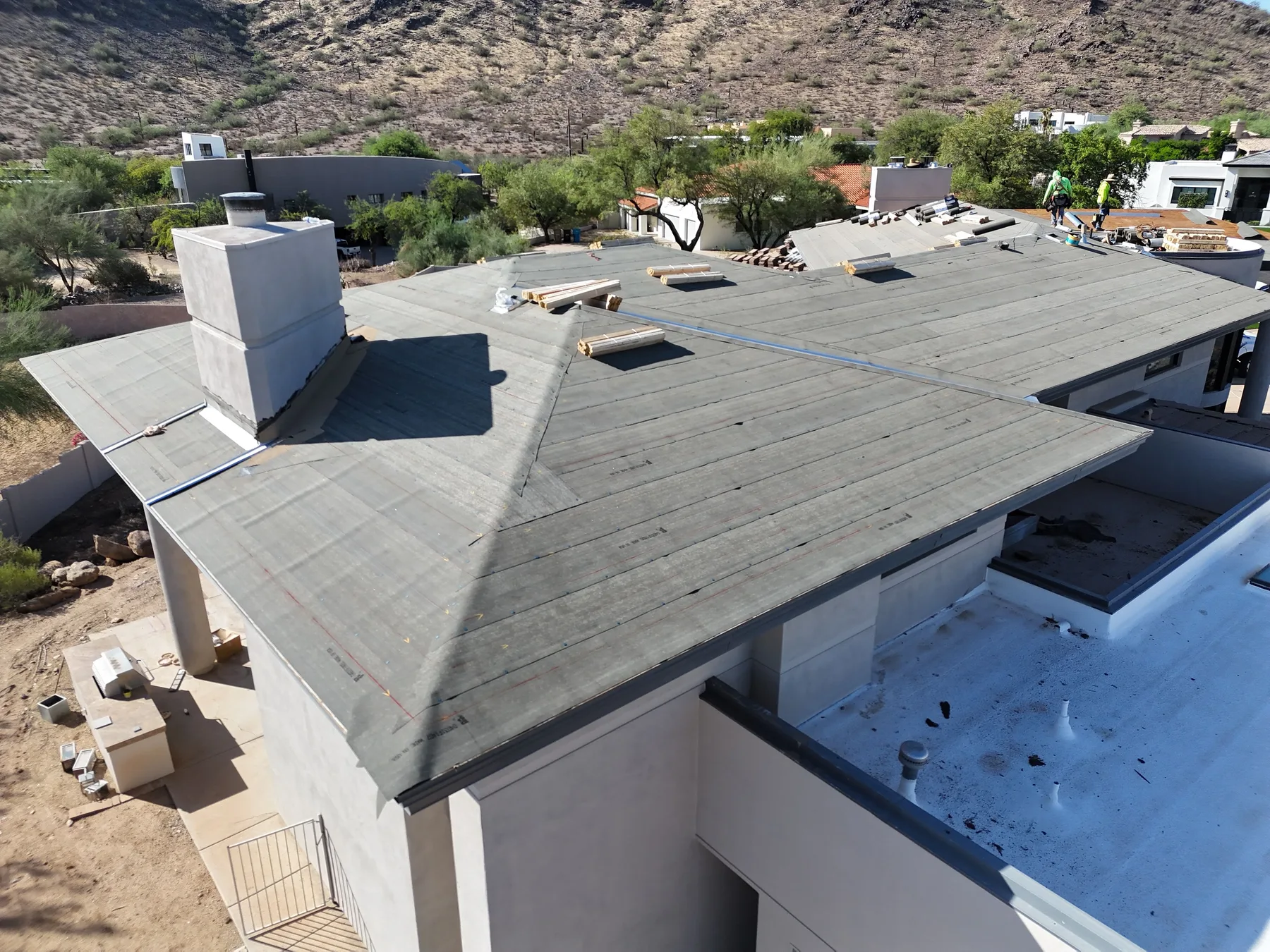 Aerial view of dark gray low-slope roofing with visible seams, chimney, and skylight