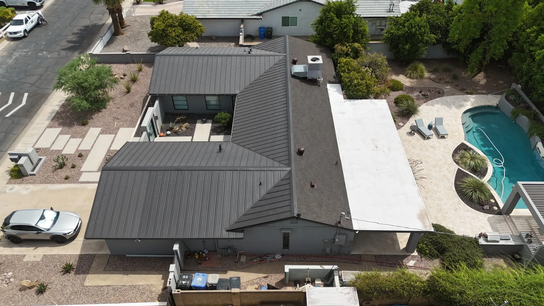 Aerial view of dark gray standing-seam metal hip roof beside a curved swimming pool