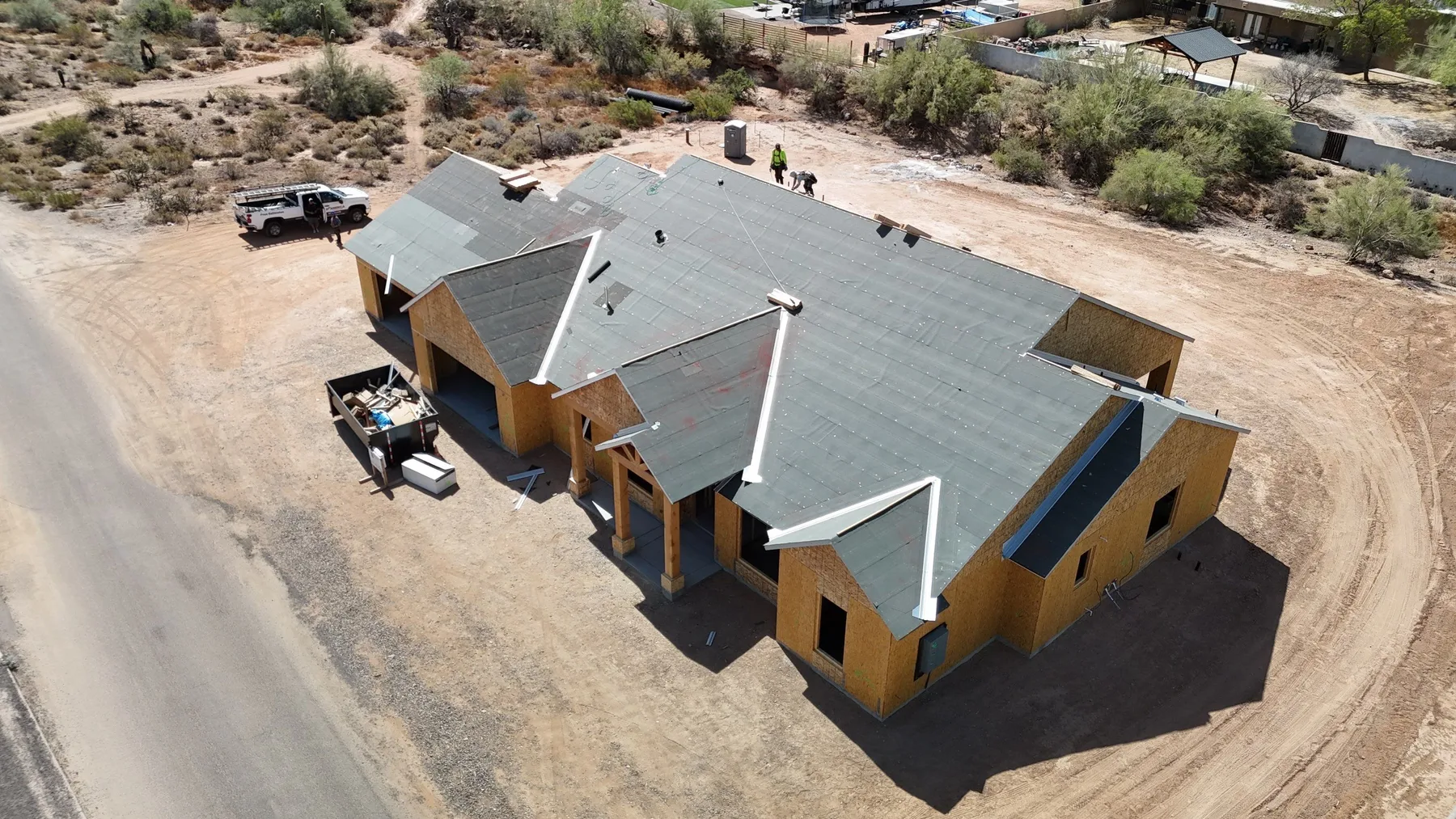 Aerial view of gray metal gable roofing on unfinished yellow house amid bare ground