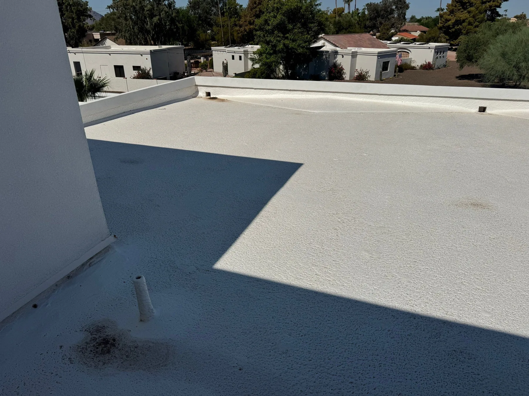 Elevated oblique view of light gray coated flat roof with parapet and vent pipe