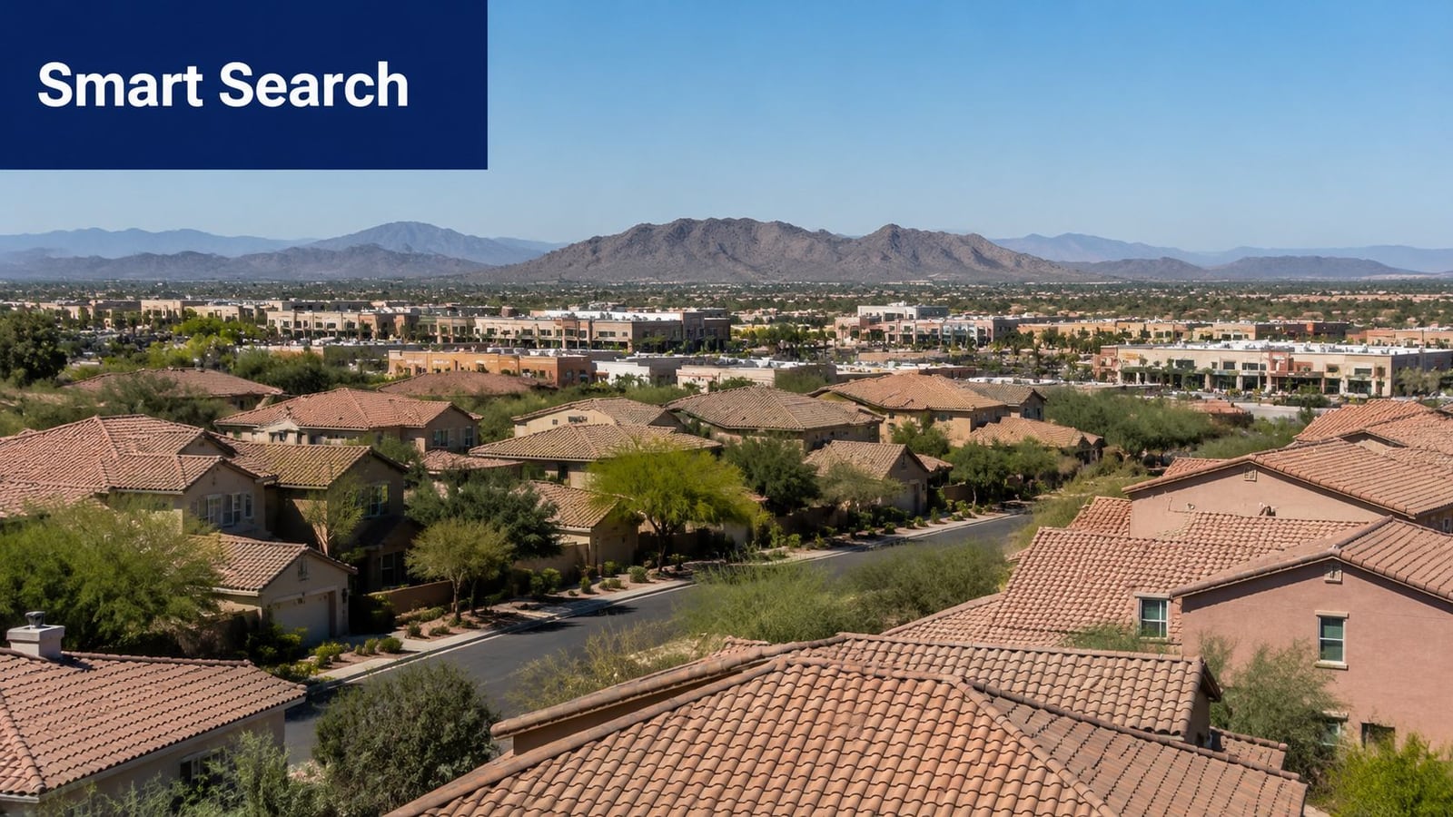 A high-angle view of a residential neighborhood with tile roofs, desert landscaping, and distant mountains.
